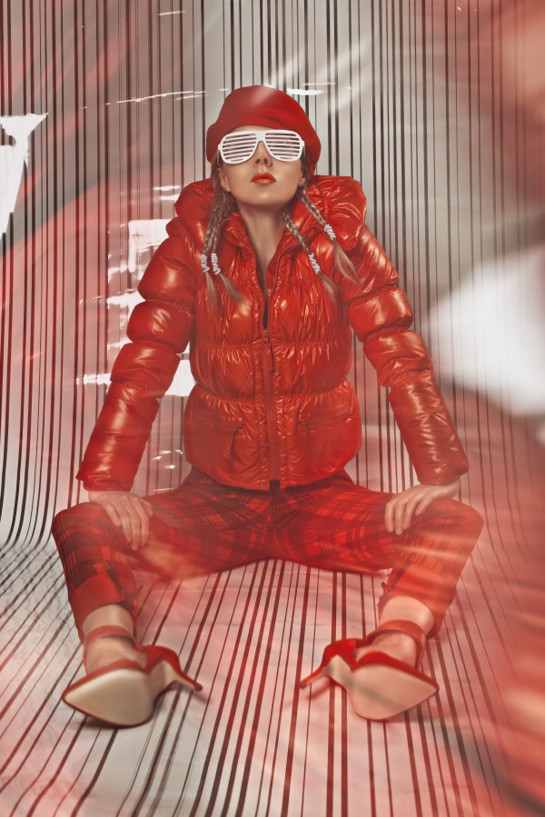 Beautiful blonde fashion model wearing braids in a red outfit with grill glasses sitting in a white striped plastic environment by Artmood Visualz